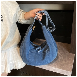 Detail of blue denim shoulder bag featuring a distressed frayed pocket and wide strap
