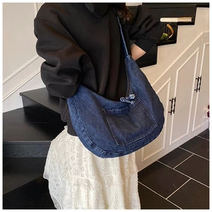 Detail of a large dark blue washed denim crescent bag worn over the shoulder by a model