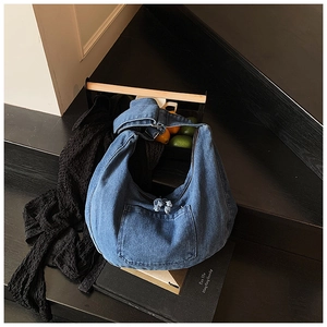 Detail of blue denim hobo bag featuring a functional front pocket and wide shoulder strap