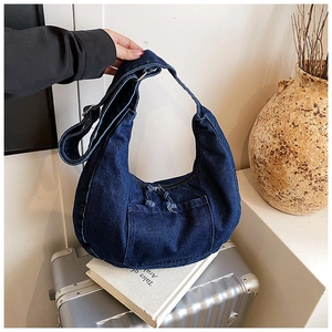 Close-up of deep blue denim crossbody bag featuring frayed zipper and front pocket detail