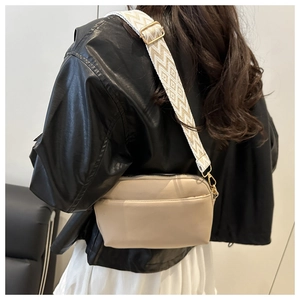 Close-up of beige square crossbody bag featuring a wide bohemian style woven shoulder strap