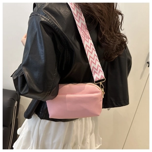 Detail of a small pink crossbody bag with a wide decorative geometric pattern strap