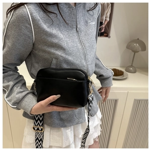 Detail of black leather crossbody bag featuring geometric wide strap and gold zipper