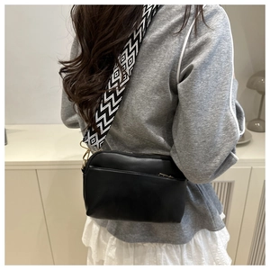 Detail of black crossbody bag with wide geometric pattern strap and gold hardware