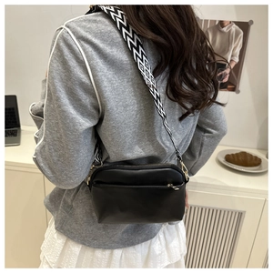 Detail of a black crossbody bag featuring a wide geometric pattern strap on model