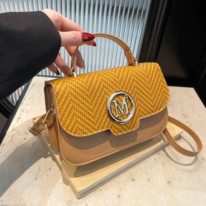 Chic women's woven crossbody bag with leather handle and silver M logo in warm studio light