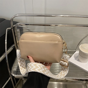 Chic beige crossbody bag with a stylish woven canvas strap and sleek gold hardware