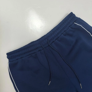 Detail of dark blue joggers with elastic waist, drawstring, and white side piping