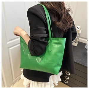 Detail of green faux leather tote bag with embossed crocodile texture worn by model