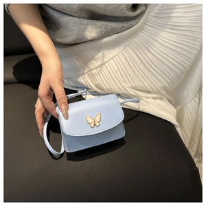 Detailed shot of mini blue leather bag with a golden butterfly buckle and slim strap
