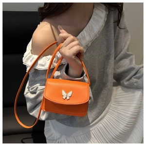 Detail view of the orange leather mini bag featuring a decorative white butterfly clasp