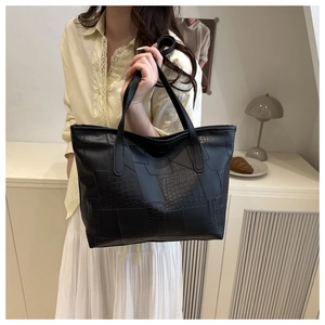 Detail of large black tote bag showing crocodile texture patchwork and spacious interior