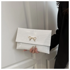 Detailed macro view of white crocodile pattern PU leather clutch with golden bow buckle