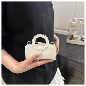 Close-up of a white mini handbag with crocodile pattern and a unique circular handle