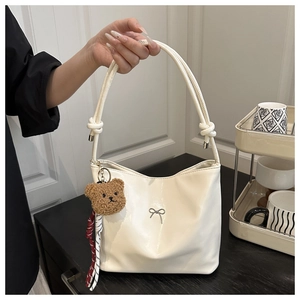 Detail of off-white glossy handbag with metallic bow accent and cute bear charm