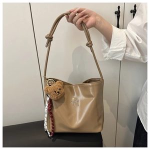 Close-up of brown faux leather tote bag featuring a silver bow buckle and plush bear charm