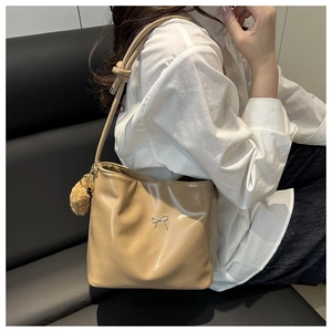 Detail of tan leather tote bag featuring a silver bow accent and brown plush charm