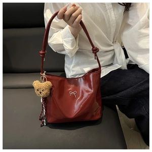 Close-up of burgundy tote bag featuring a silver bow accent and cute plush bear charm
