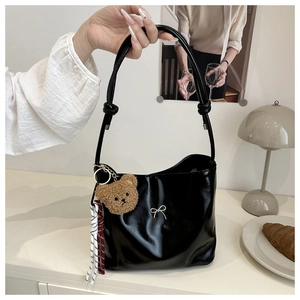 Detail of black patent leather tote featuring a silver bow and plush bear charm