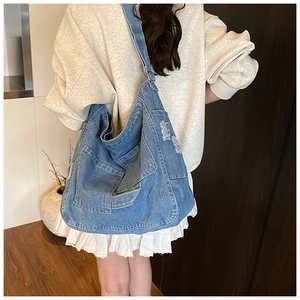 Detail of washed denim tote bag with vintage distressed holes and large front pocket