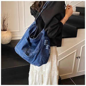 Detail of large blue denim tote bag with washed texture and multiple utility pockets