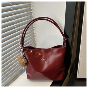 Detail of burgundy glossy tote bag featuring a silver bow and plush bear charm