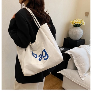 Macro detail of white canvas tote bag with front pocket featuring blue 'bag' lettering