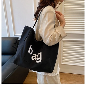 Detail of black canvas tote bag showing the bold white bag print and fashion side label