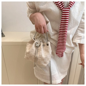 Detail of beige checkered bucket bag with silver butterfly charm and chain strap