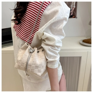 Detail of cream straw bucket bag featuring silver chain and butterfly metal pendant charm