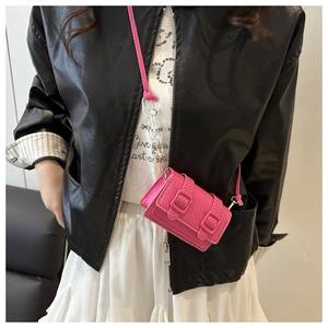 Detail of pink mini textured leather crossbody bag with dual buckles on a model