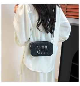 Detail of black sequined camera bag with silver rivet SM logo and wide fabric strap
