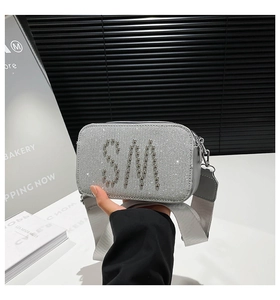 Close-up of silver glitter camera bag featuring studded SM initials and wide fabric strap