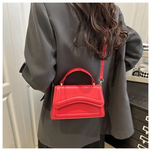 Detail view of the vibrant red chic crossbody bag worn with a tailored charcoal suit blazer