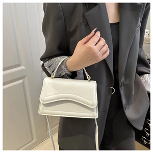 Detailed view of white minimalist handbag featuring unique layered wave flap design
