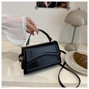 Detail of black leather handbag with wave stitching and gold hardware on a desk