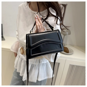 Detail of black glossy PU leather handbag with wavy stitching and gold hardware