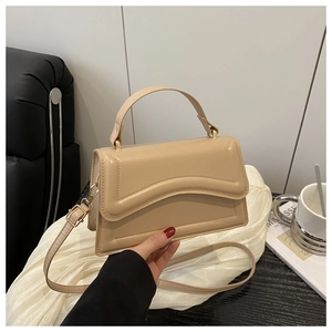 Detail of a chic beige structured handbag featuring a wave pattern flap on a minimalist background