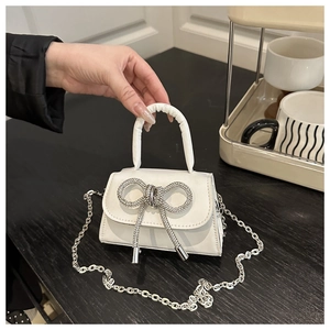 Close-up van witte mini-handtas met fonkelende strass-strik en zilveren kettingdetail