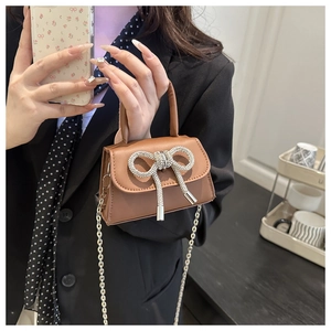 Detailoverzicht van bruine mini-tas met glinsterende strass-strik en fijne metalen ketting