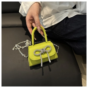 Detail van neongele mini-tas met kristallen strik en zilveren kettingriem