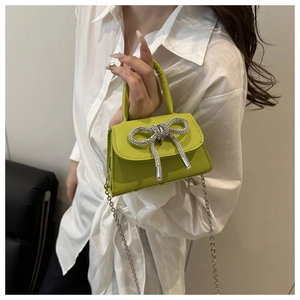 Detail van een mini groene leren tas met glanzende strass-strik en een zilveren kettingriem