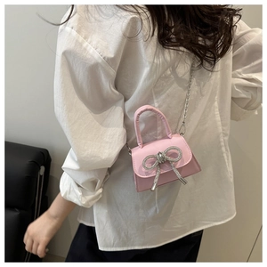Detail van een roze mini-crossbodytas met zilveren strass-strik en een metalen ketting