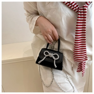 Detail van een zwarte matte mini-tas met grote zilveren strass-strik en ketting