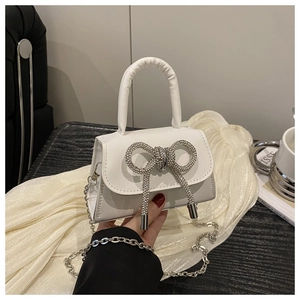 Detail van witte mini handtas met strass-strik en zilveren ketting schouderriem