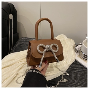Detail van bruine PU-tas met fonkelende strass-strik en zilveren kettingriem