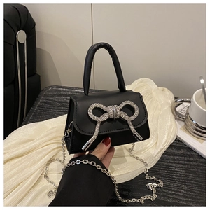 Detail van zwarte PU-handtas met sprankelende zilveren strass-strik en een kettingriem