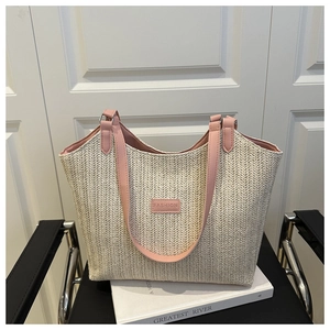 Détail du tissage en paille beige avec étiquette en cuir rose sur un grand sac cabas d'été