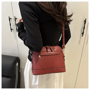 Detail of burgundy woven crossbody shell bag with gold hardware shown on a model