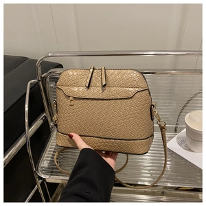 Detail of beige woven shell bag with gold hardware and adjustable strap in a lifestyle setting